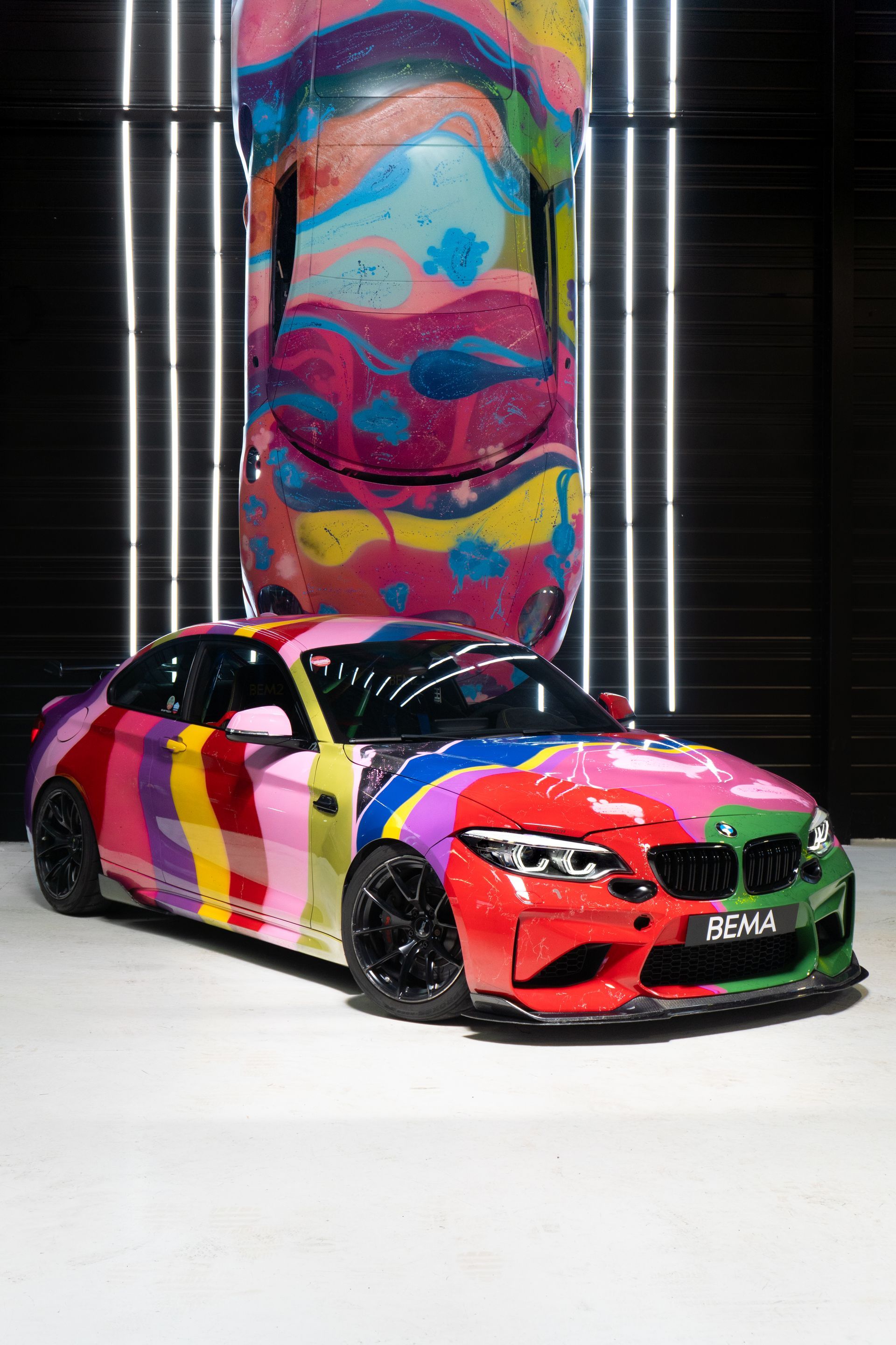 Voiture coupé BMW M2 personnalisée et colorée avec une voiture assortie en arrière-plan dans un studio.