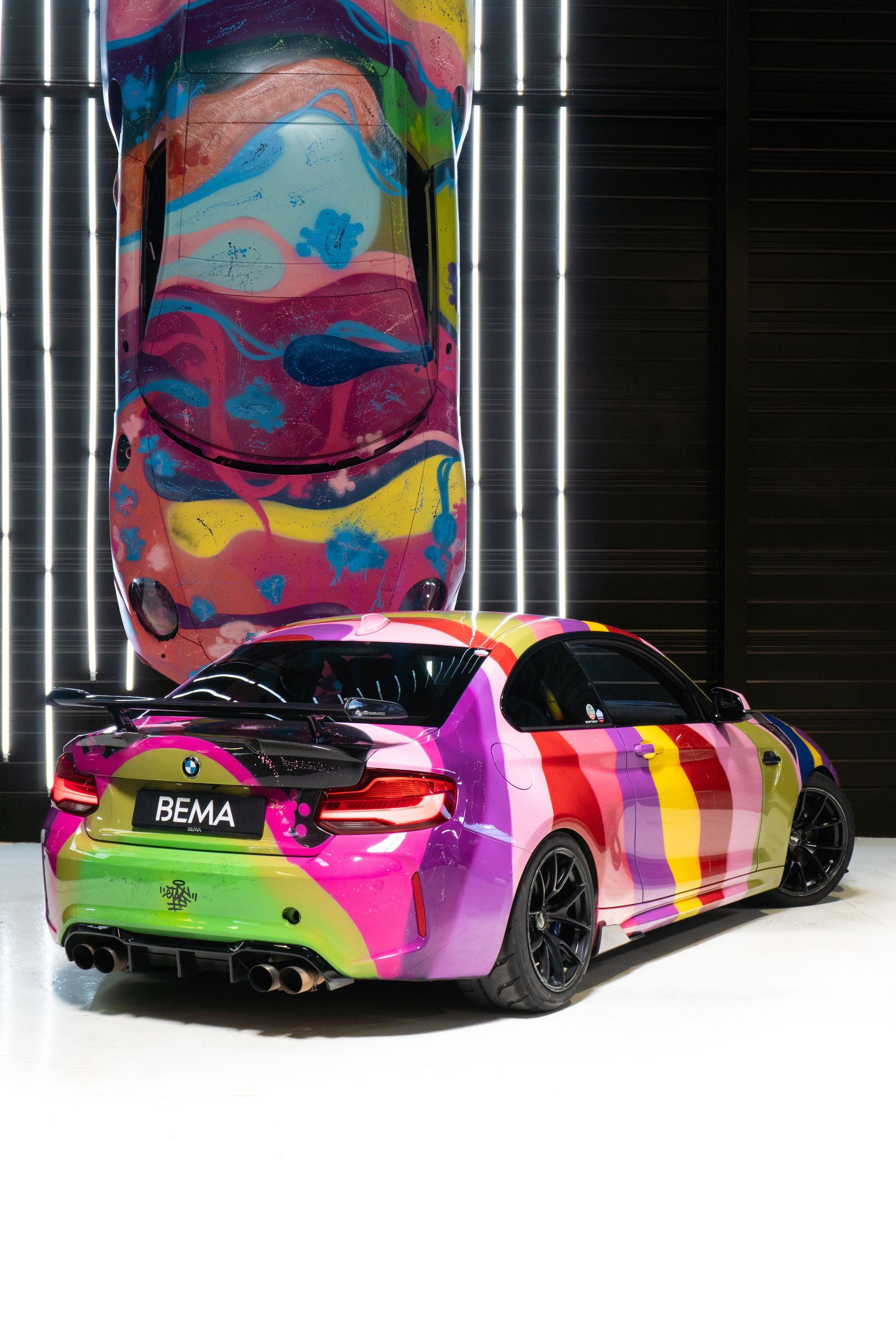 Voiture de sport BMW colorée avec une voiture assortie exposée, côte à côte dans une salle d'exposition.