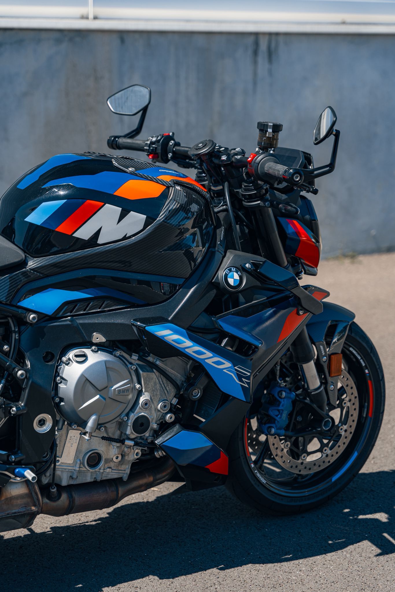 Moto BMW M 1000 R, accents bleus, blancs et rouges, garée à l'extérieur par une journée ensoleillée.