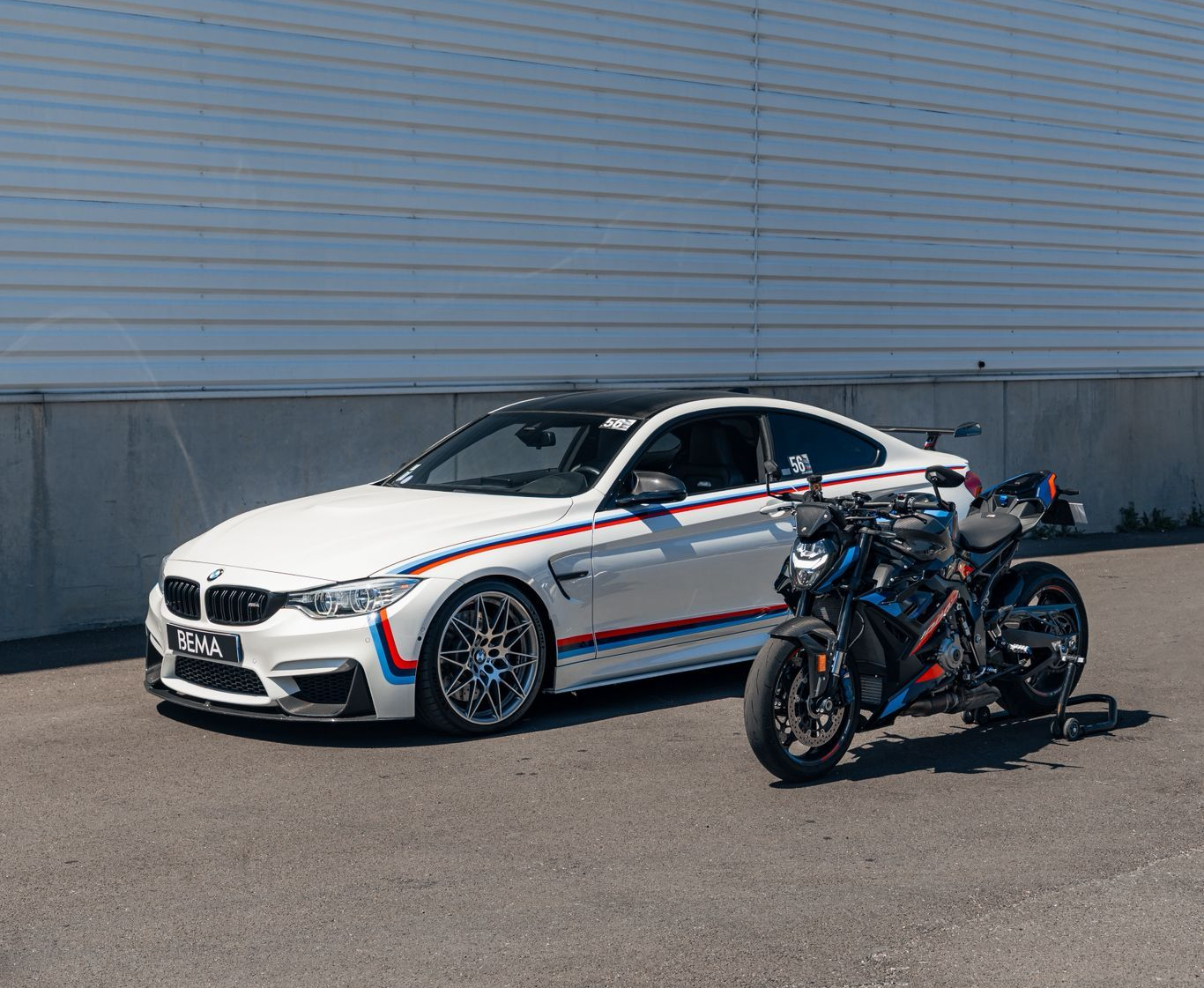BMW M4 blanche et moto noire avec des accents bleus garées sur l'asphalte.