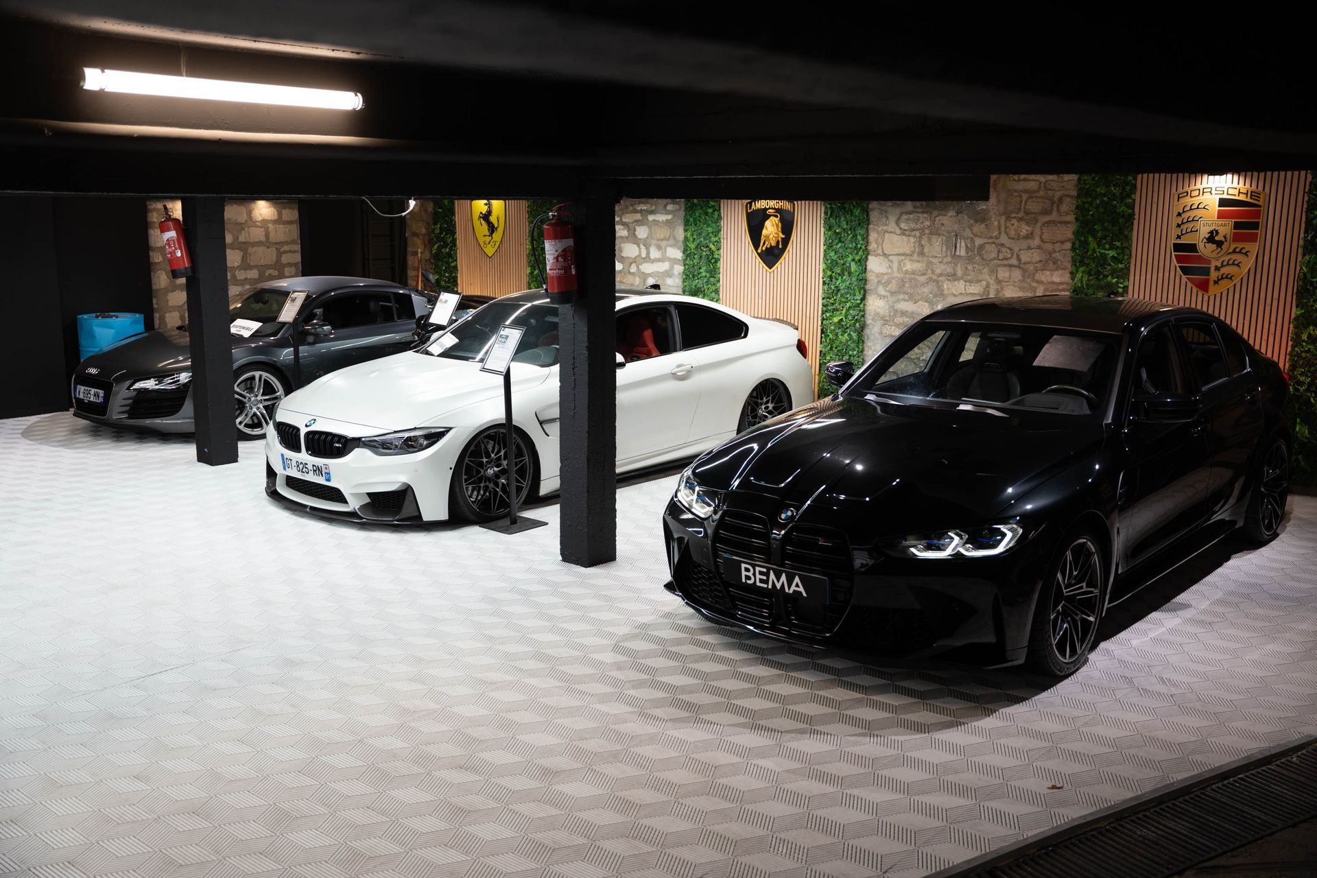 Voitures exposées dans une salle d'exposition : véhicules noirs, blancs et gris avec des accents colorés.