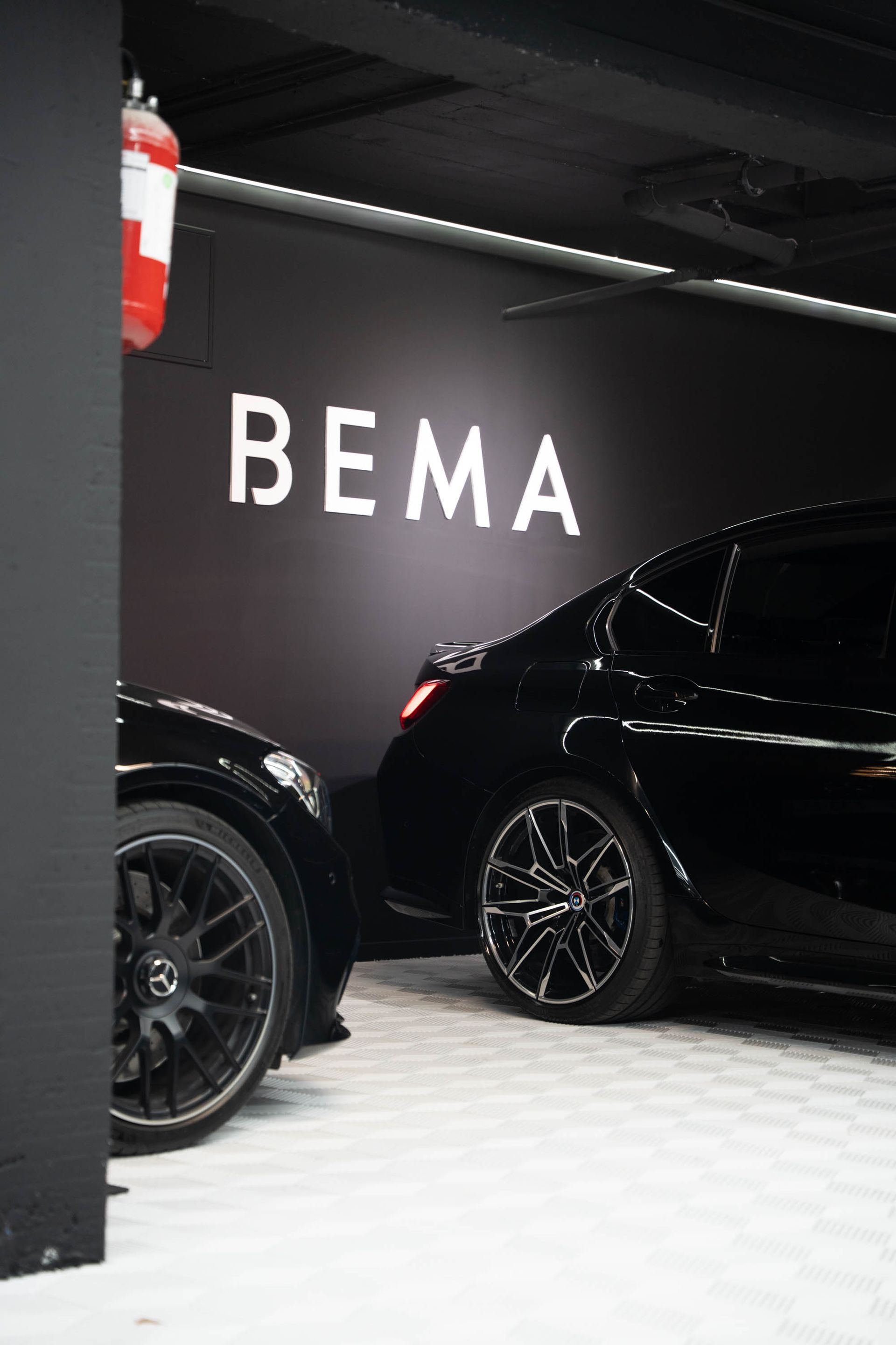 Voitures noires garées devant un panneau « BEMA » sur un mur noir ; un extincteur est visible.