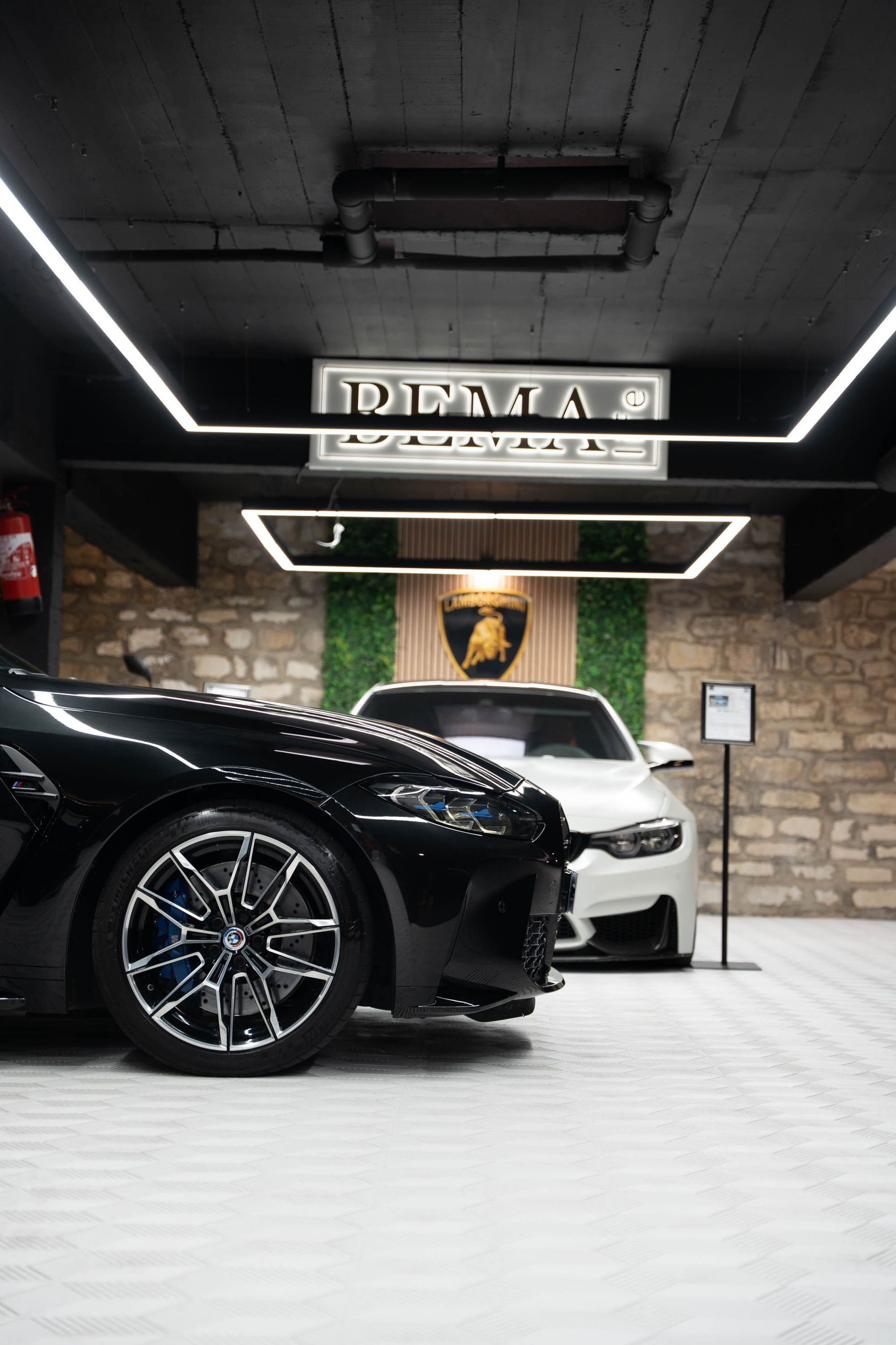 Voiture noire garée à côté d'une voiture blanche à l'intérieur d'un garage, sous le panneau « DETAILING ».