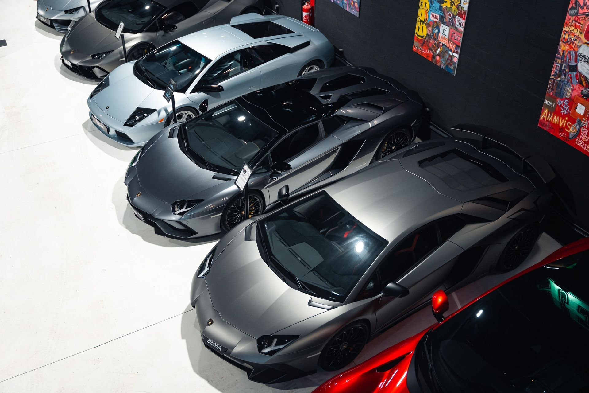 Voitures de luxe, dont des voitures de sport argentées, grises et rouges, garées dans un garage avec des affiches.