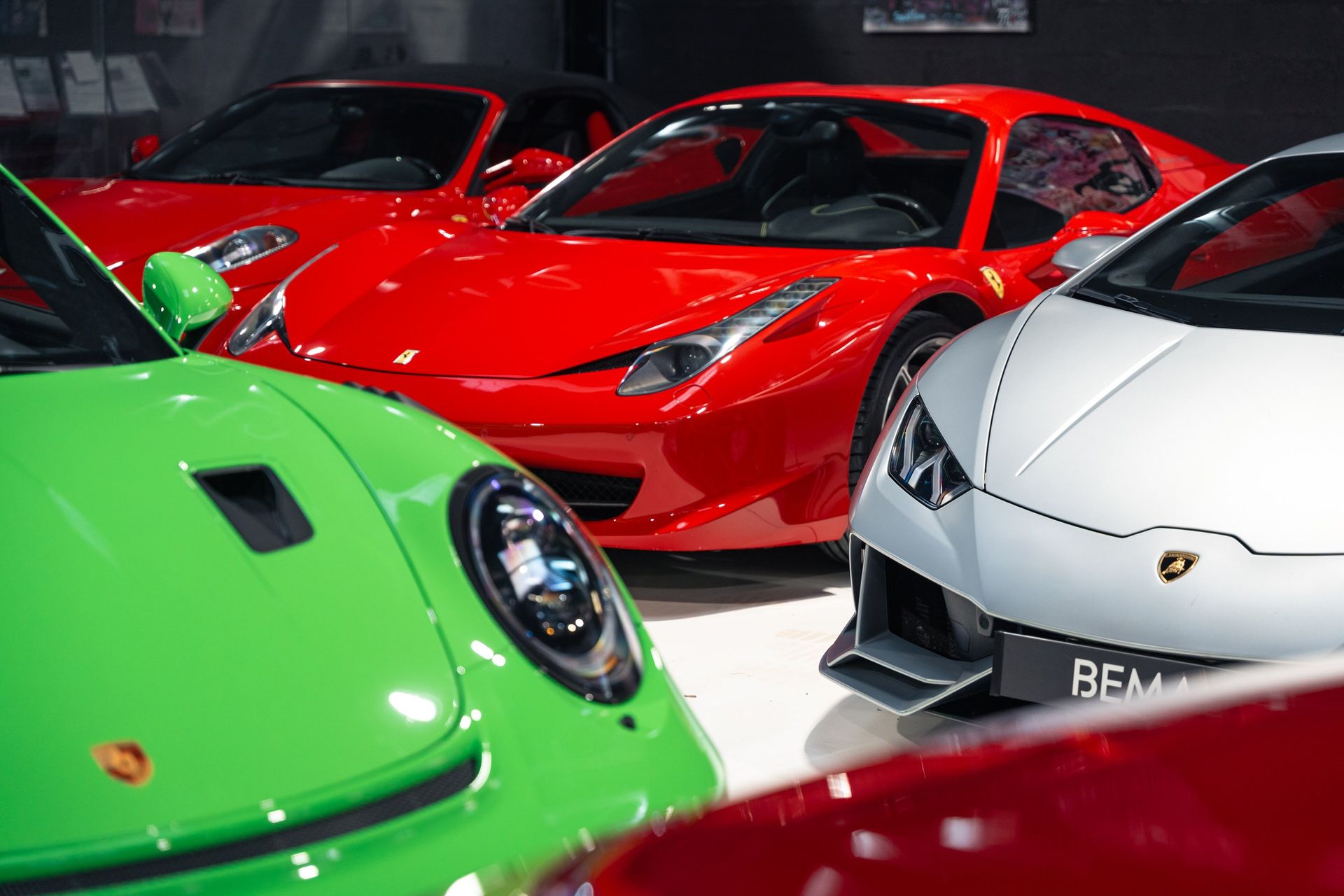 Voitures de sport lumineuses en vert, rouge et blanc garées dans une salle d'exposition.