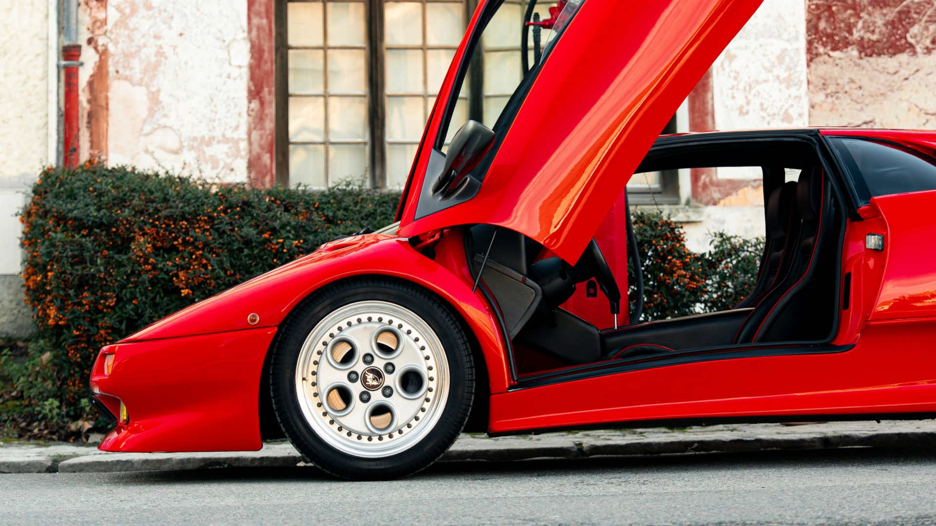 Voiture de sport rouge, portes ouvertes, garée devant un bâtiment.