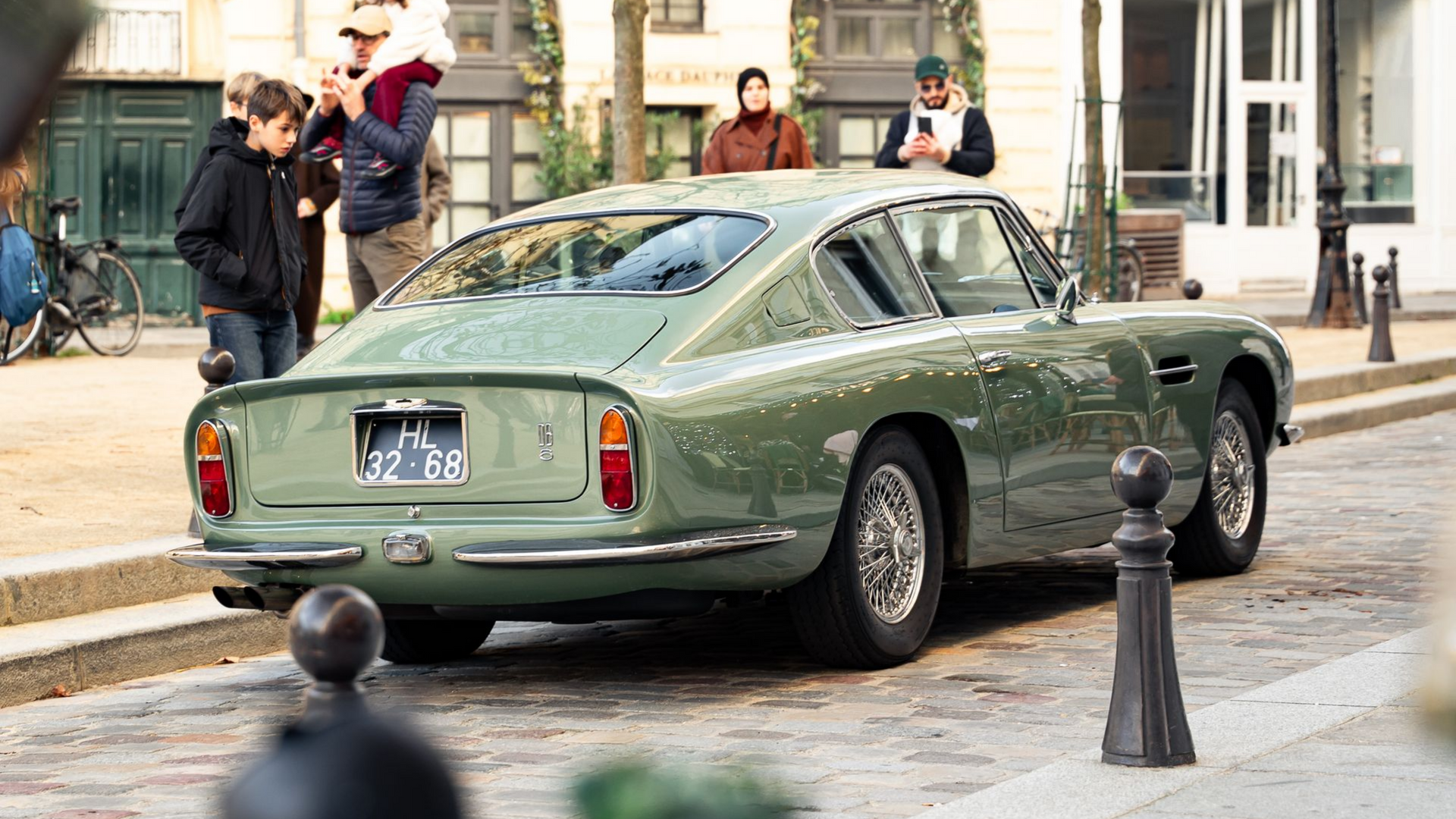 Voiture classique verte garée dans une rue parisienne, avec des passants en arrière-plan.