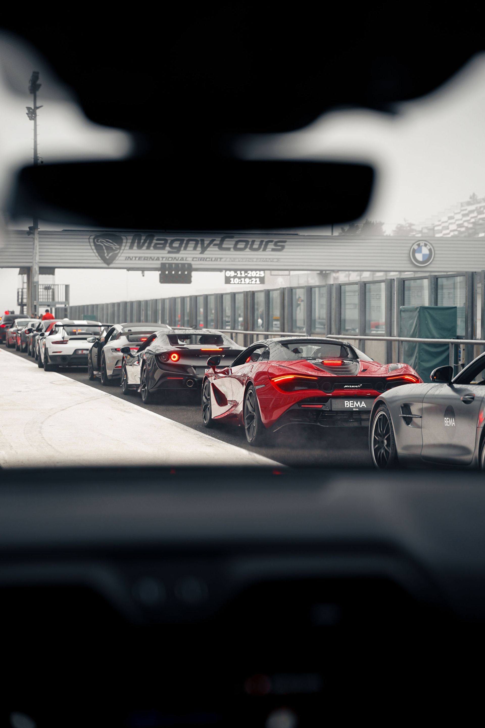 Lamborghini argentée sur une route, suivie d'autres voitures, arbres sur les côtés, montagnes en arrière-plan.