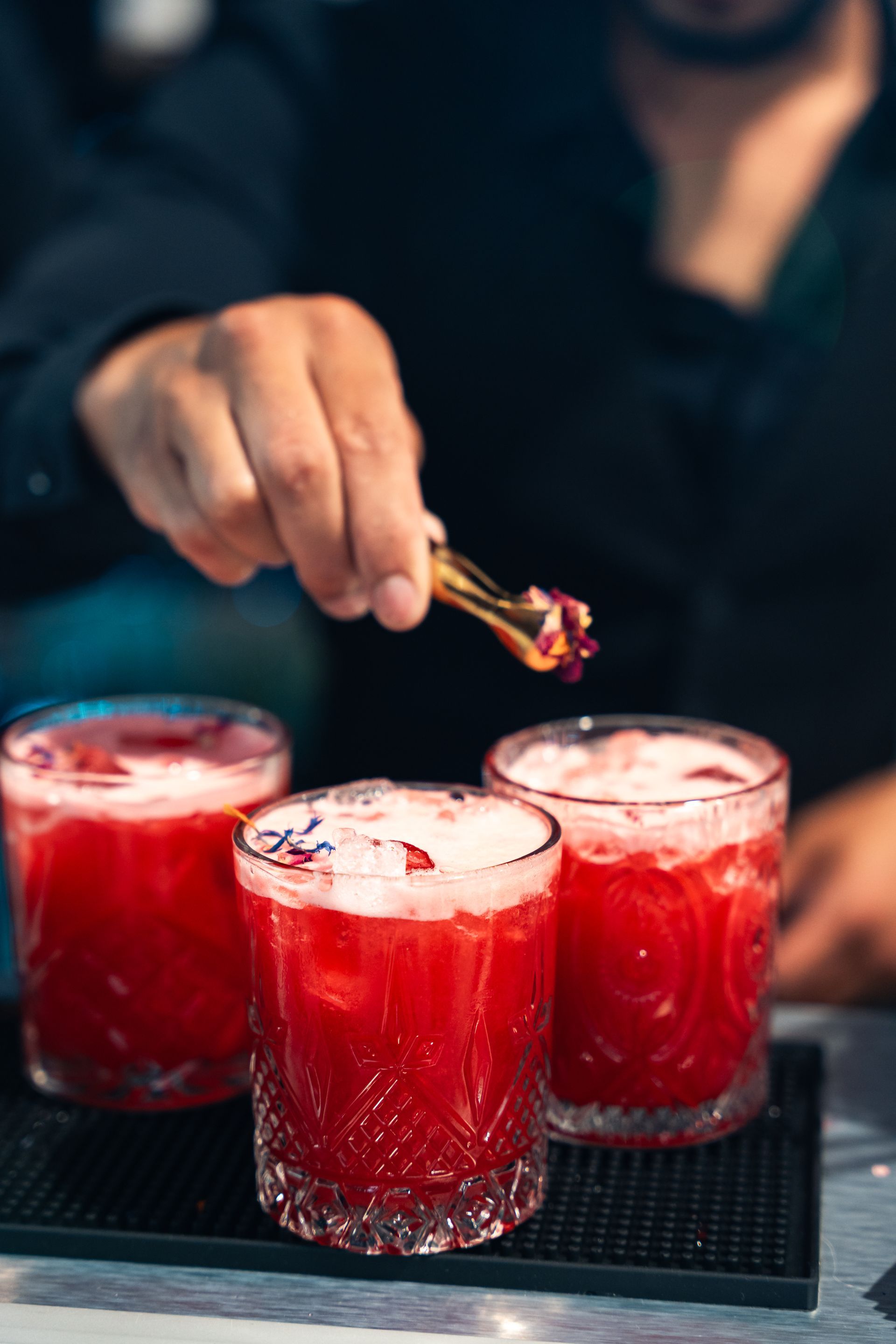 Le barman garnit trois cocktails rouges de pétales de fleurs.