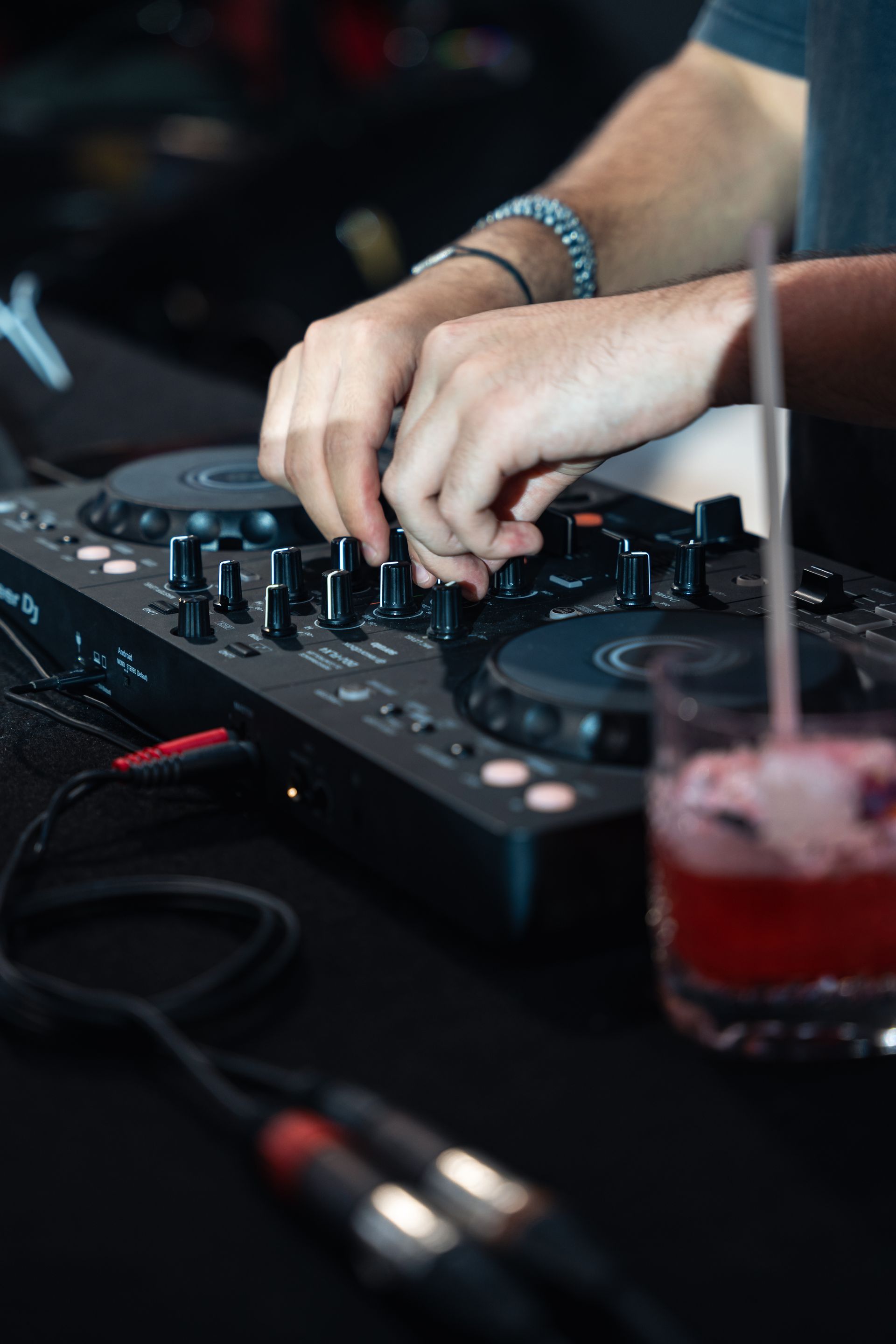DJ au travail, mains manipulant le mixeur audio avec une boisson au premier plan.