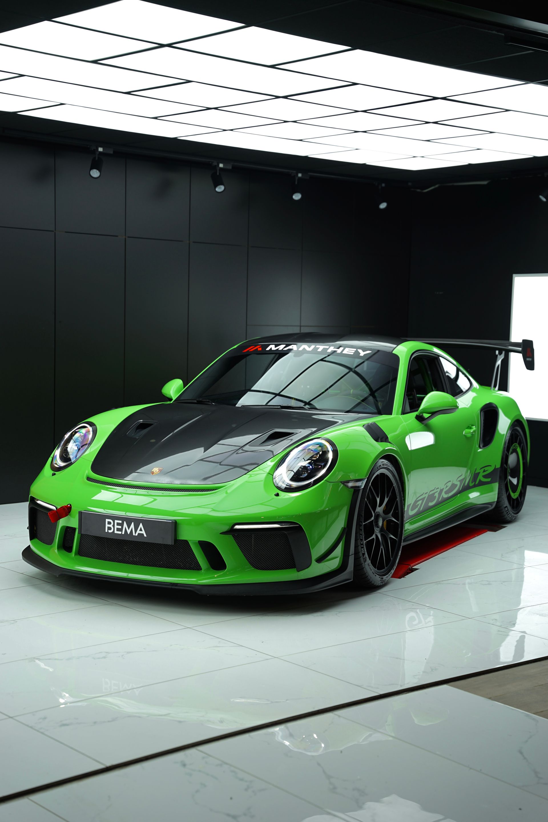 Porsche 911 GT3 RS verte avec capot et aileron noirs, dans une salle d'exposition.
