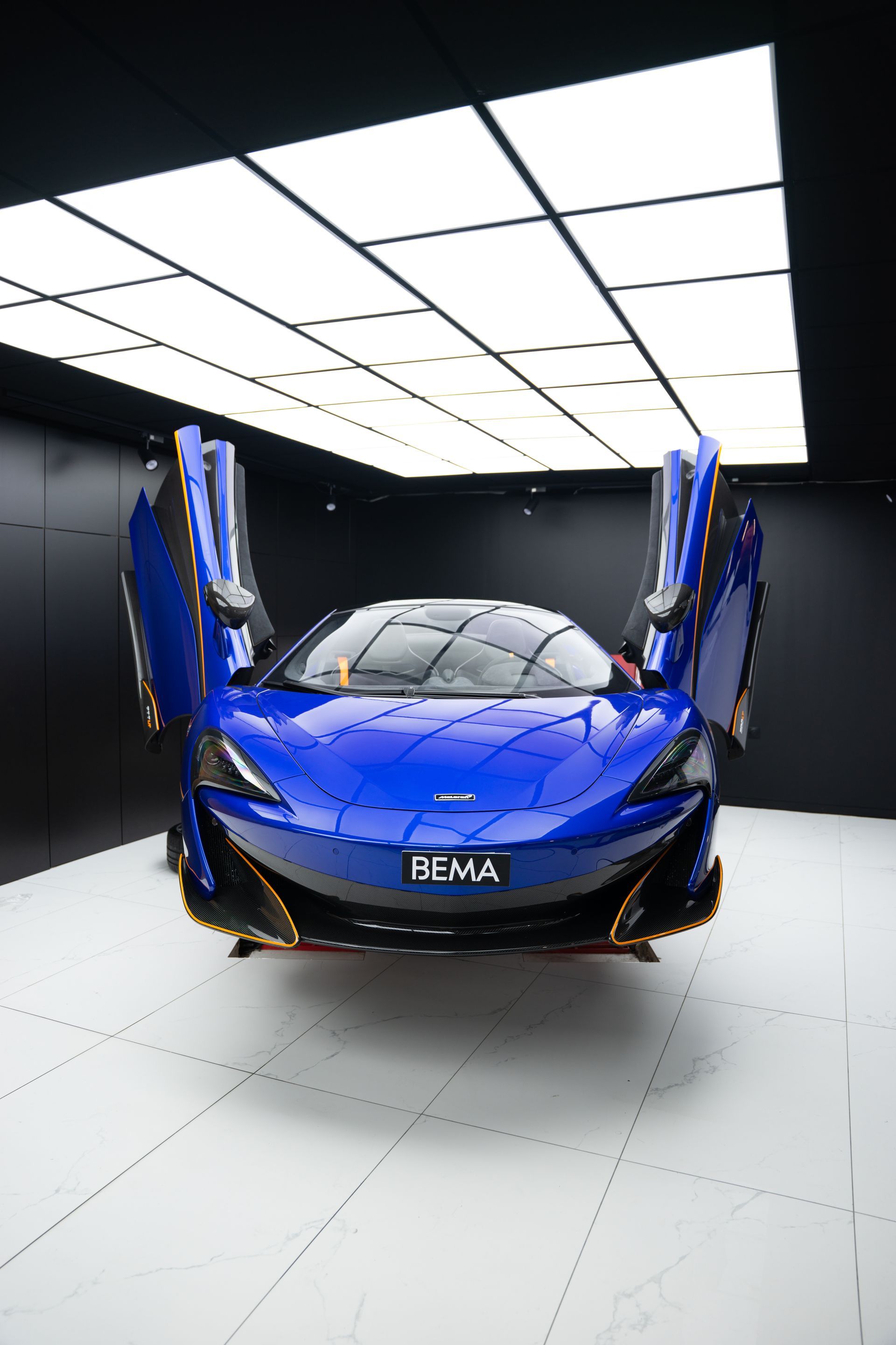 Voiture de sport McLaren bleue, portes ouvertes, dans un showroom.