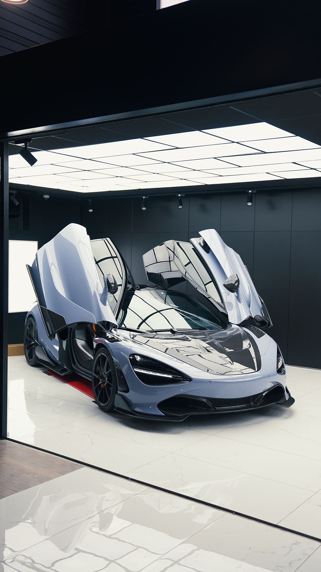 Personne appliquant un film protecteur sur une voiture noire à l'aide d'outils et portant des gants noirs.