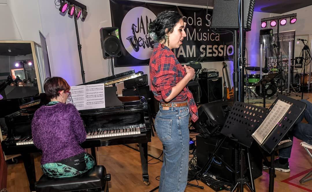 Una mujer canta en un micrófono mientras otra mujer toca el piano.