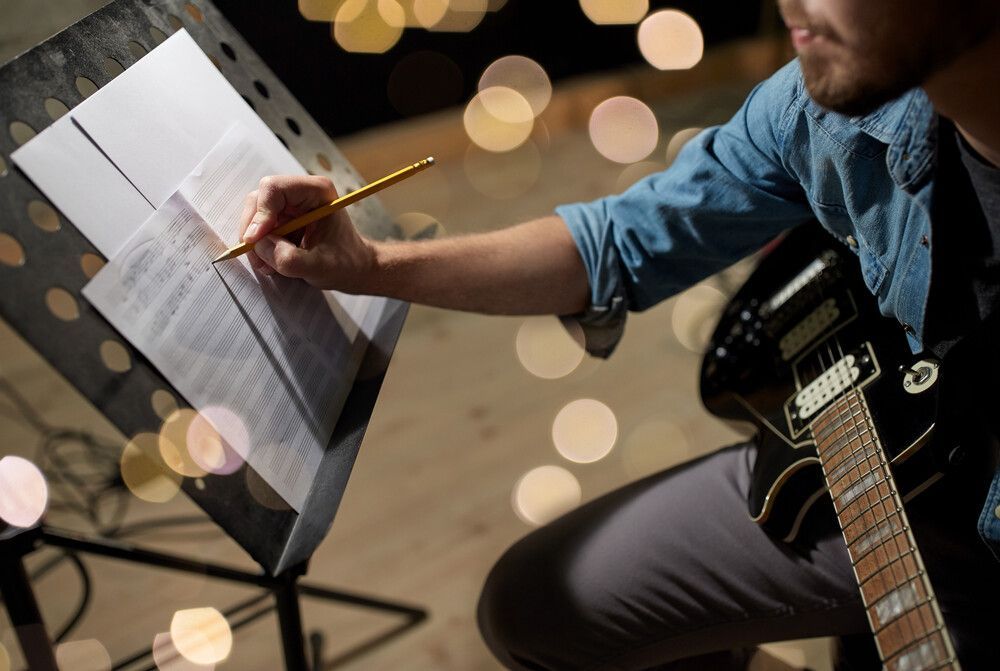 Un hombre toca una guitarra y escribe música en un atril.