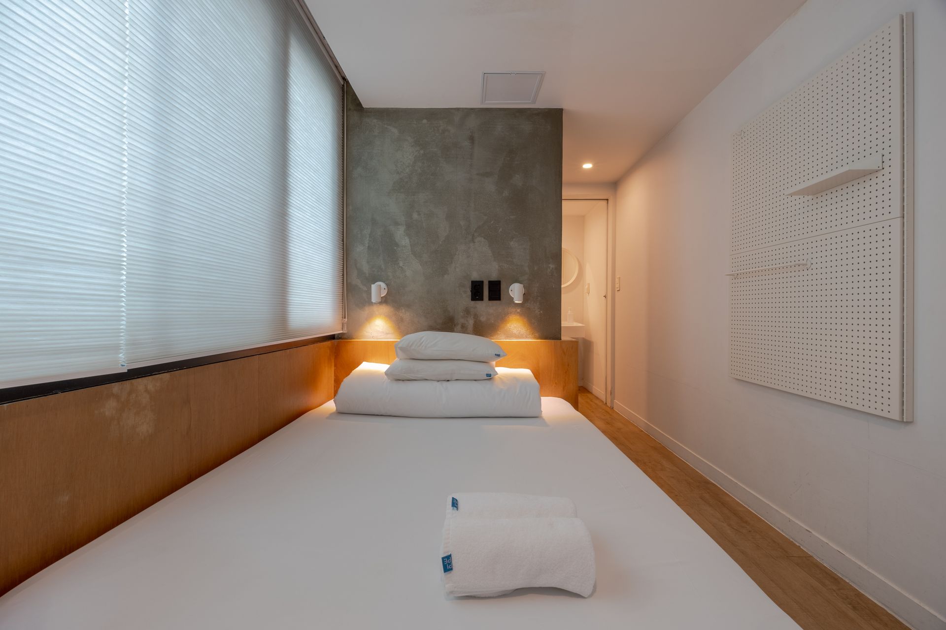 Modern hotel room with a bed, brick wall, and a hallway leading to a door. PIPE Hostel Yeonnam