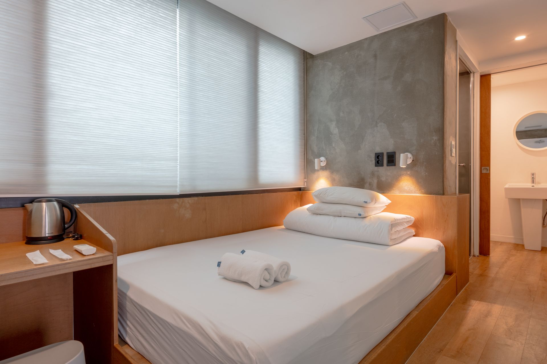 Bedroom with large window, bed, and minimalist decor; gray walls, white bedding, and small bedside table.