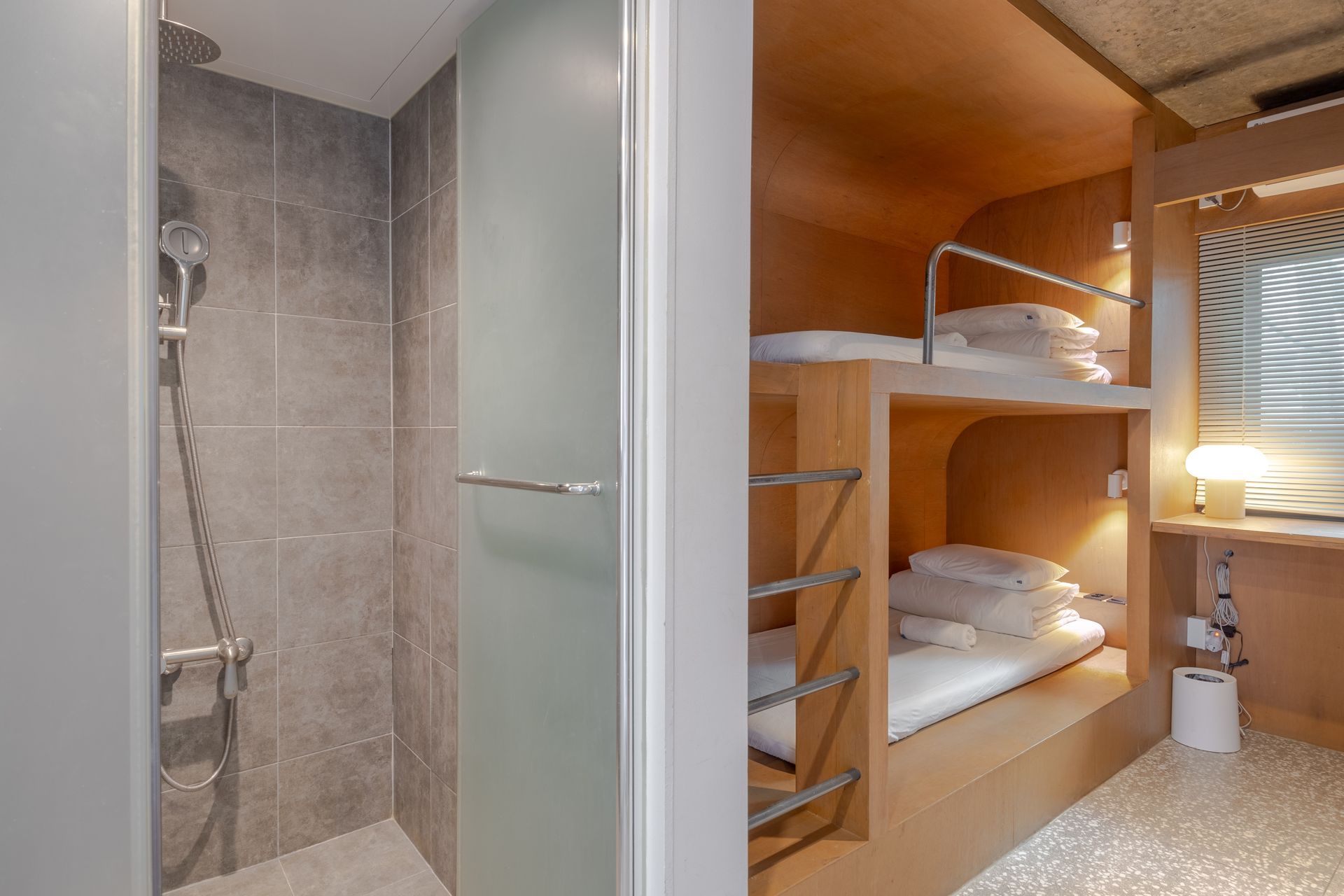 Bunk beds in a room with a attached bathroom. Beige and white interior with a window.