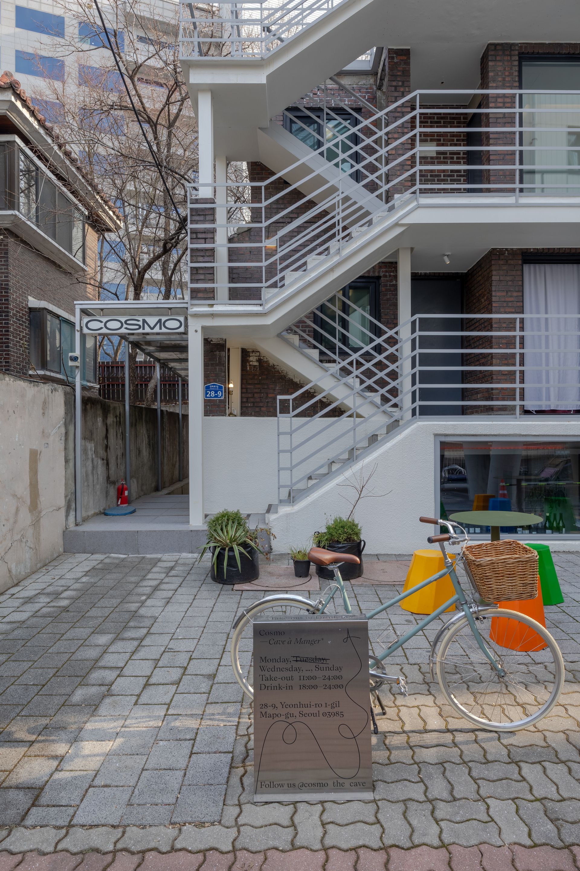 PIPE Hostel. Modern white building with external stairs, brick facade, and small outdoor tables.