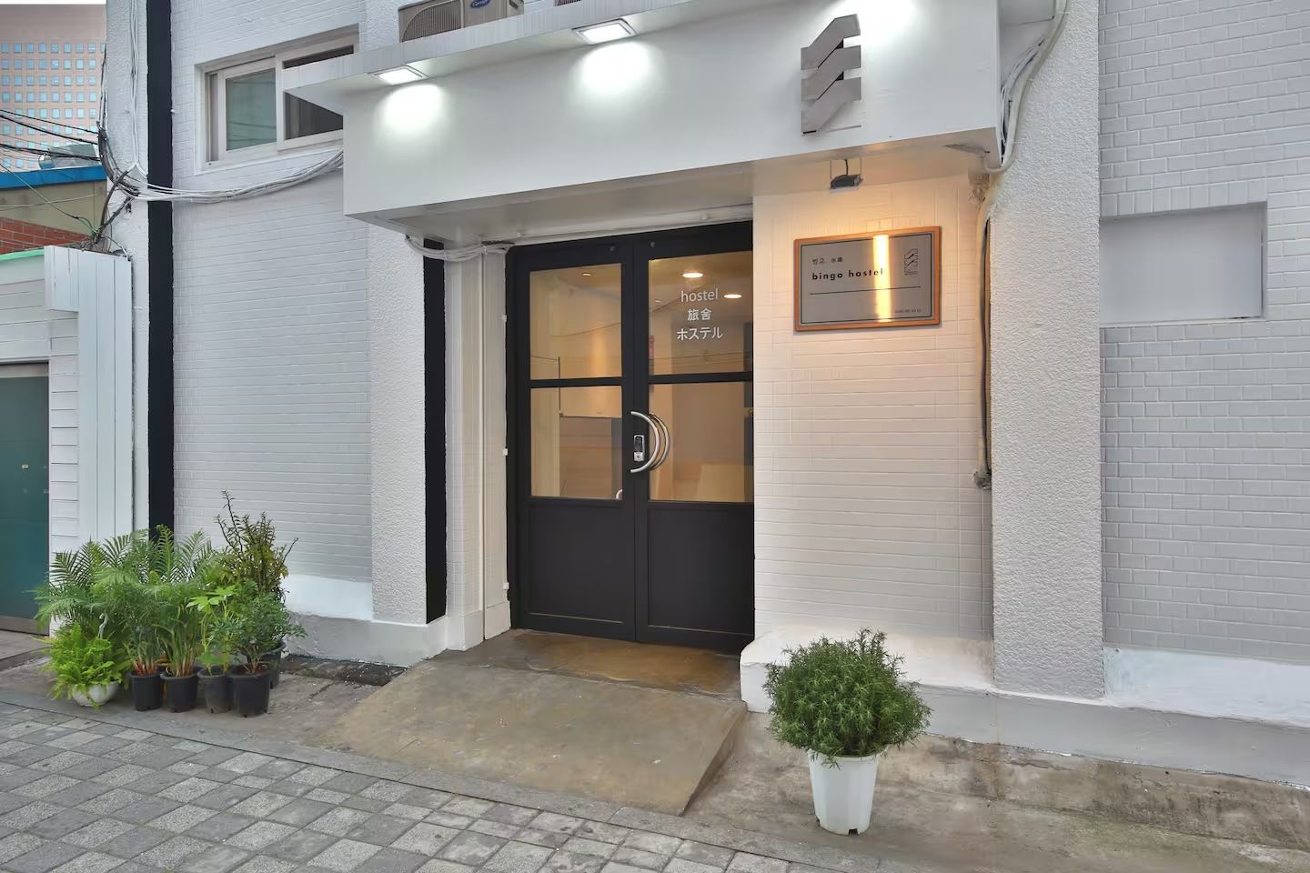 White building entrance with black doors, small potted plants, and a ramp for accessibility.