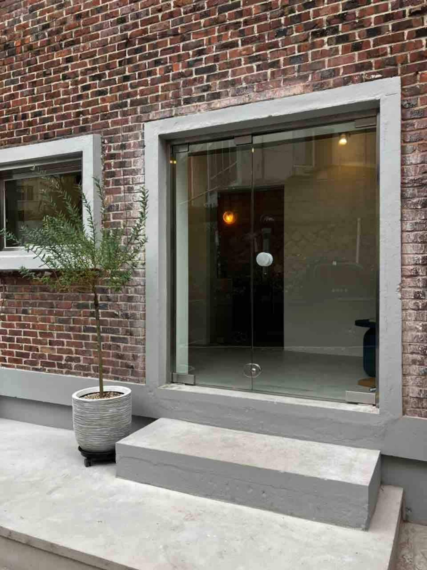 Glass door entrance with gray steps and brick wall; a potted plant sits beside the door.