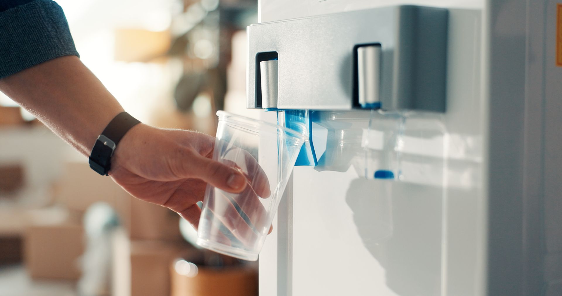 Gros plan sur une main tenant un gobelet en plastique sous le distributeur d'une fontaine à eau.