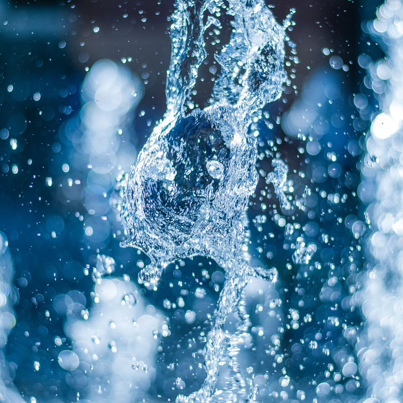Capture en gros plan et à haute vitesse de gouttes et de ruisseaux d'eau bleue éclatante sur un fond sombre et flou.