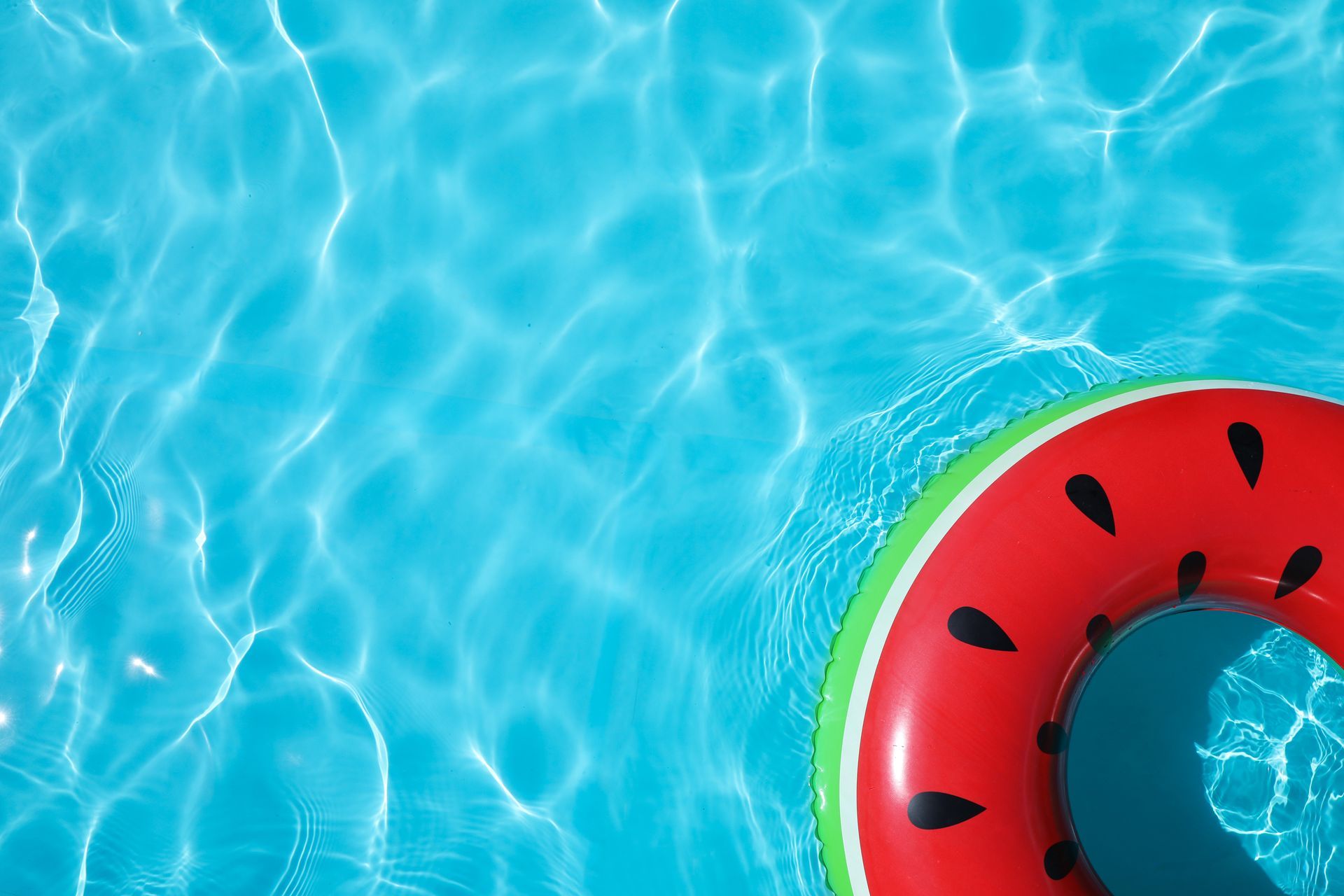 Une bouée de piscine à motif de pastèque flotte à la surface de l'eau bleue, calme et ondulante.