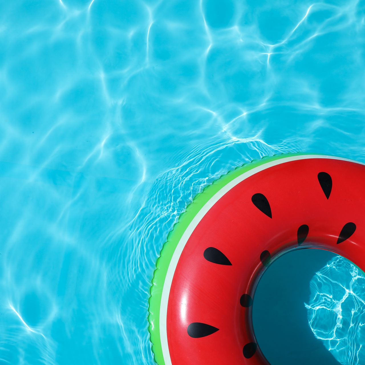Une bouée de piscine à motif de pastèque flotte à la surface d'une eau bleu vif et ondulante.