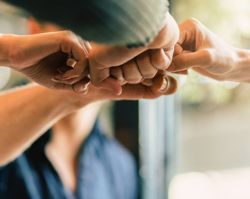 Gros plan sur plusieurs mains se rejoignant dans un poing levé unifié, symbolisant le travail d'équipe et la coopération.