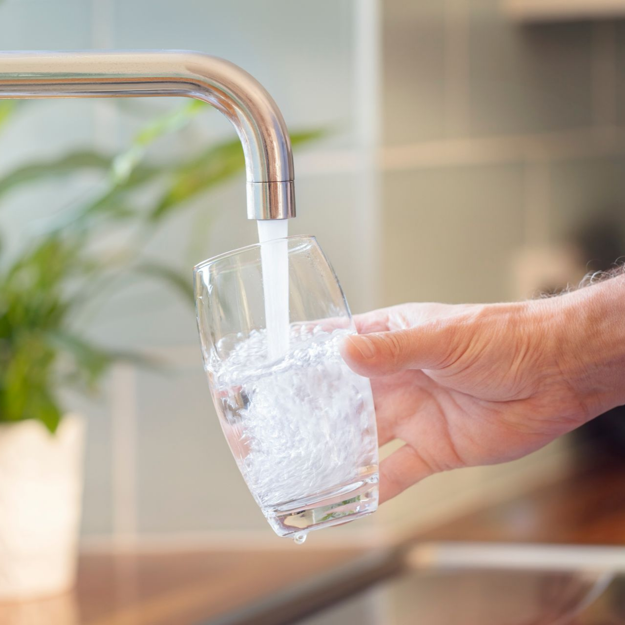 Une personne tenant un verre transparent sous un robinet de cuisine, le remplissant d'eau courante.