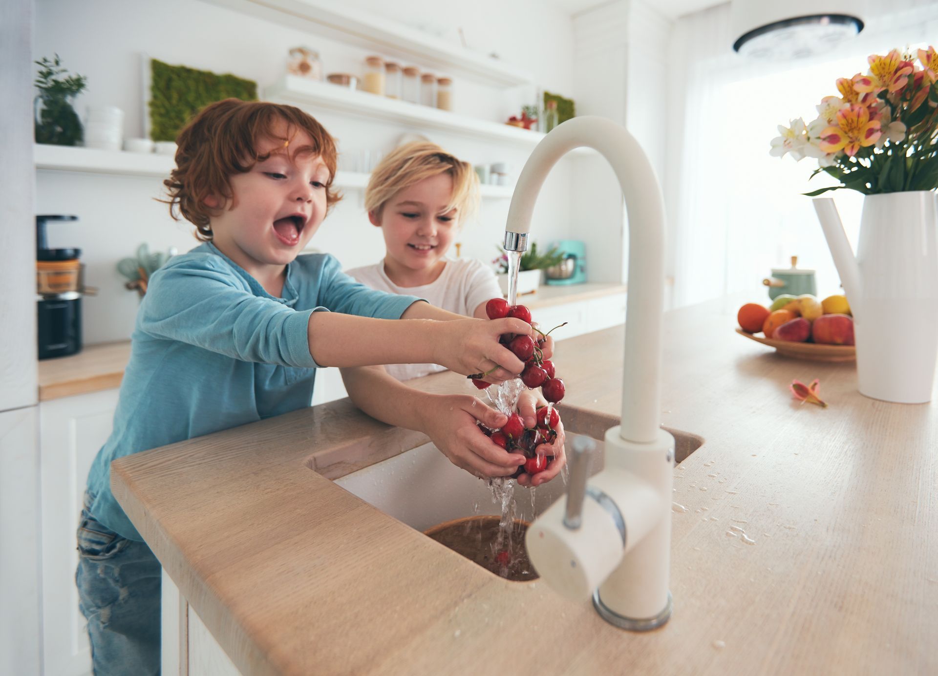 Deux enfants lavent joyeusement une poignée de cerises fraîches sous le robinet de la cuisine.