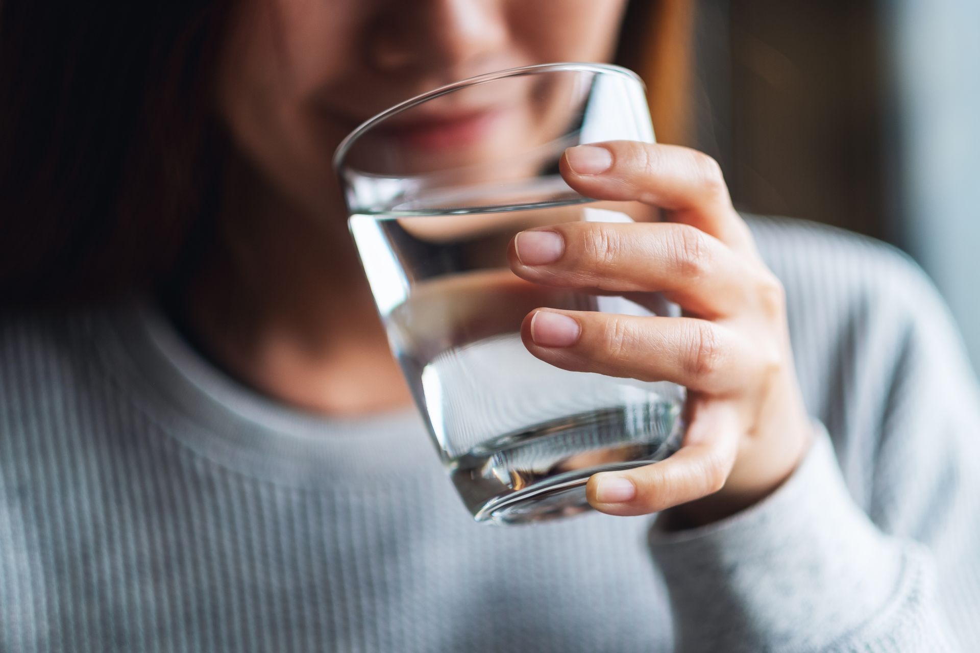 Gros plan sur une personne tenant un verre d'eau transparent près de sa bouche.
