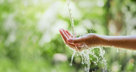 De l'eau claire se déverse sur une main ouverte, les gouttelettes éclaboussant un fond naturel vert vif et flou.