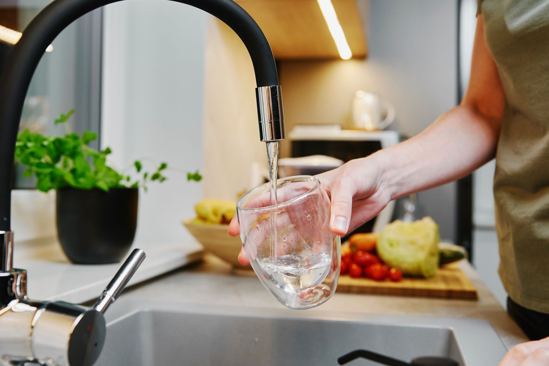 Dans une cuisine contemporaine et lumineuse, une personne remplit un verre transparent d'eau provenant d'un robinet de cuisine moderne et noir.