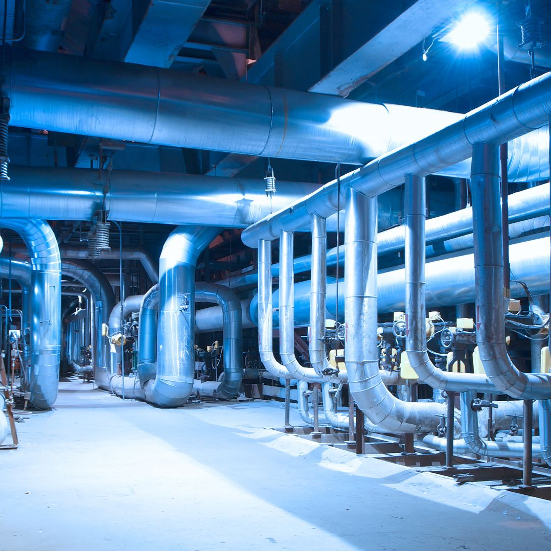 Installation industrielle caractérisée par un réseau complexe de grands tuyaux argentés éclairés dans une ambiance froide aux tons bleutés.