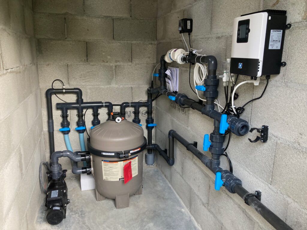 Un système de filtration pour piscine comprenant une pompe, un filtre à sable beige et un contrôleur électronique, monté sur un mur en blocs de béton.