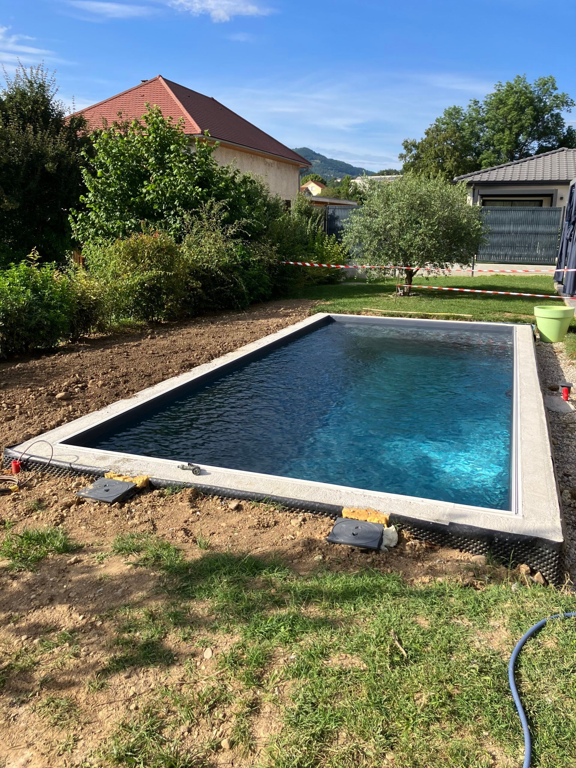Une piscine rectangulaire aux eaux d'un bleu profond, entourée de margelles en pierre claire, située dans une cour sous un ciel bleu.