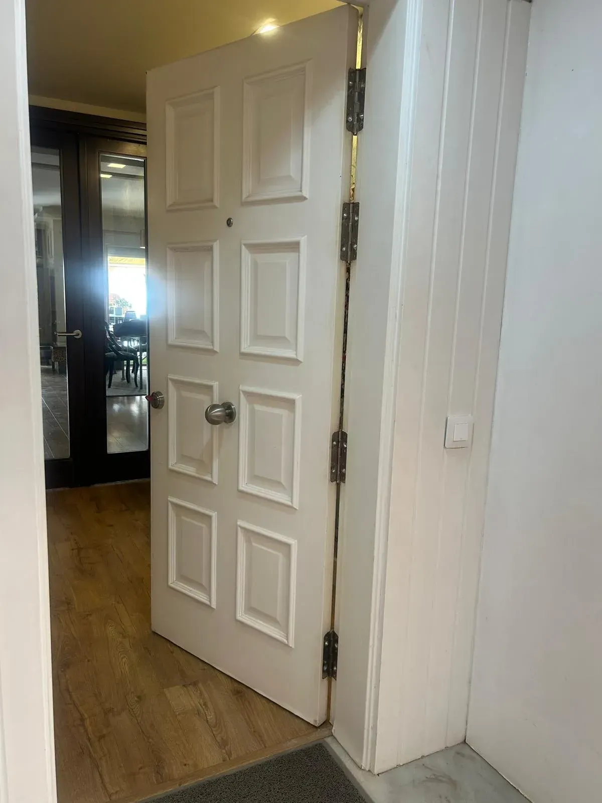 Puerta blanca abierta en un pasillo con suelo de madera y un espejo en la pared.
