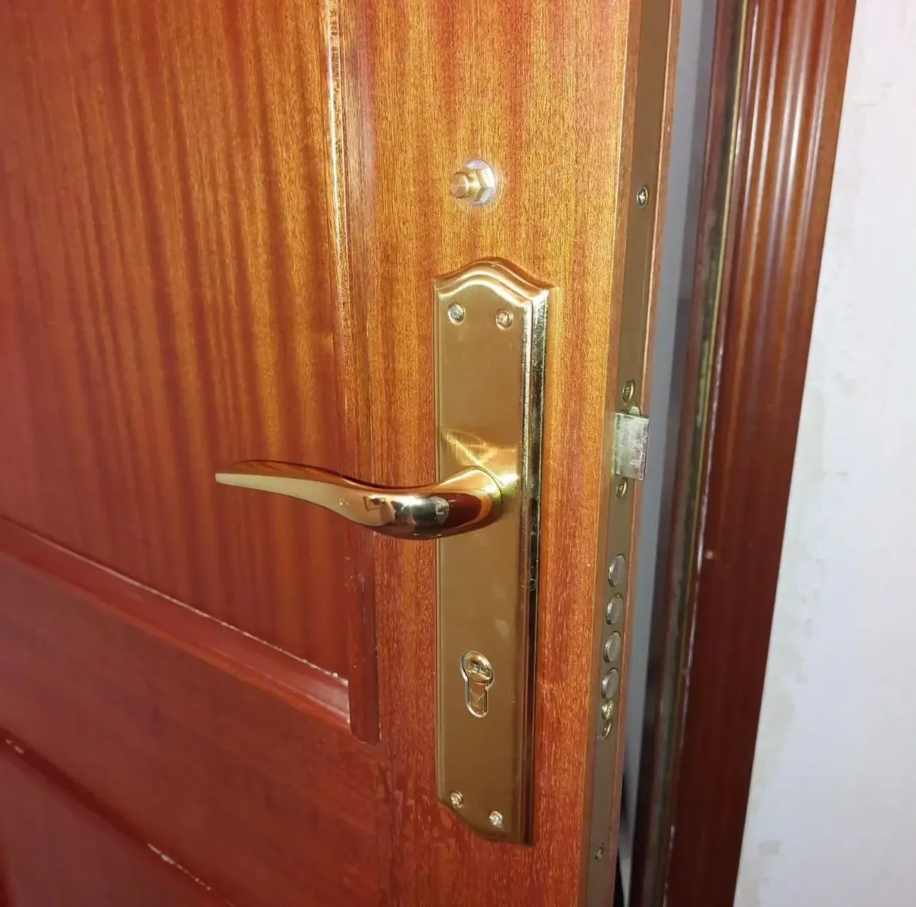Primer plano de una puerta de madera con manija y cerradura de latón ligeramente abiertas.