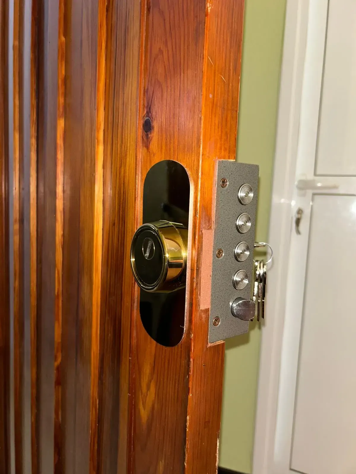 Primer plano de una puerta de madera con pomo de latón y herrajes de cerradura metálicos visibles en el borde.