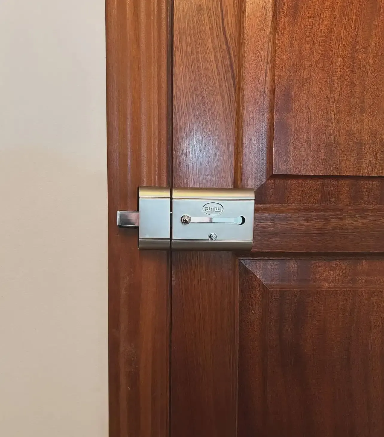 Primer plano de un pestillo de puerta plateado en una puerta de madera marrón con una pared beige.