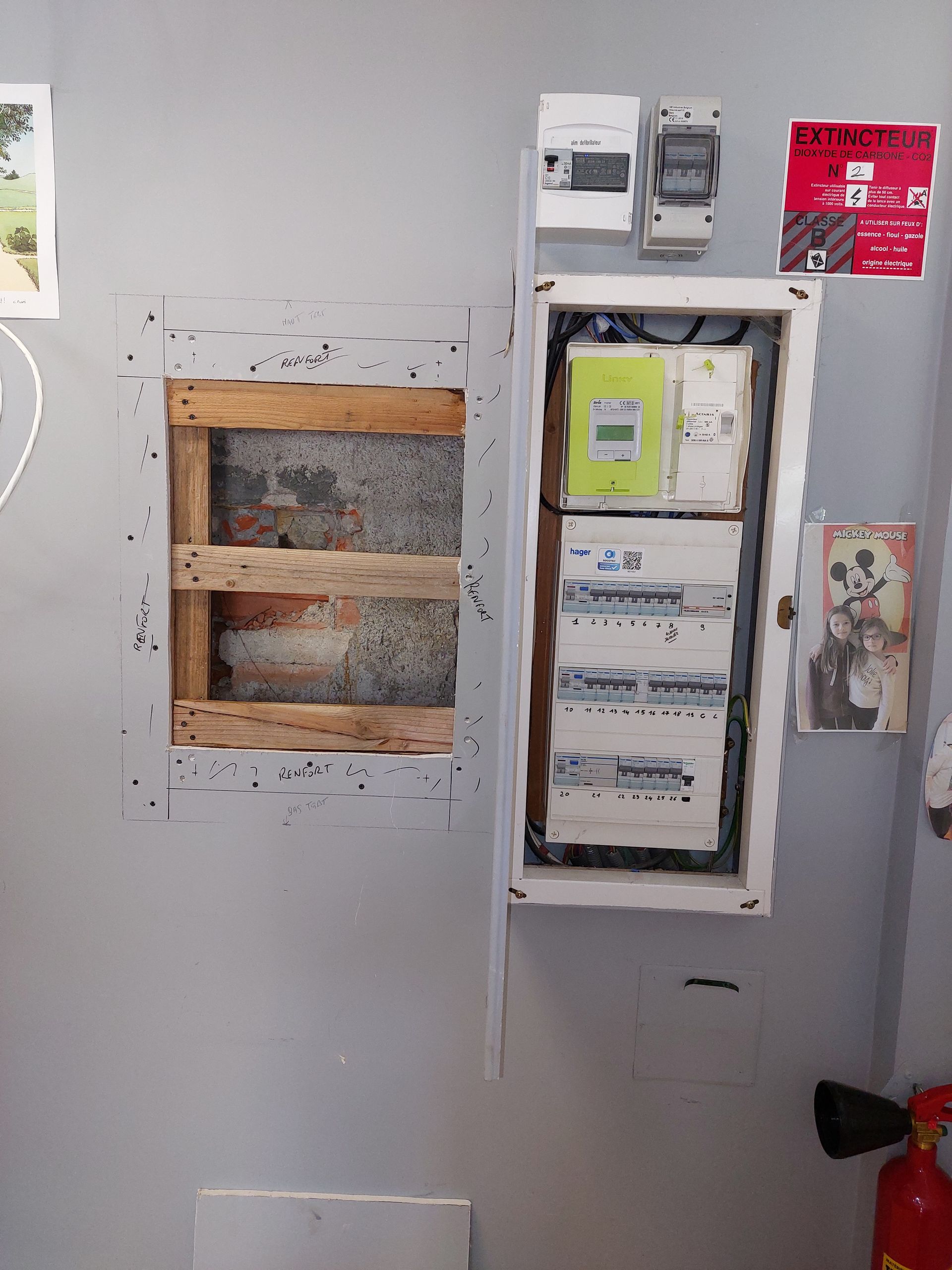 Tableau électrique encastré dans un mur gris, à côté d'un cadre en bois vide.