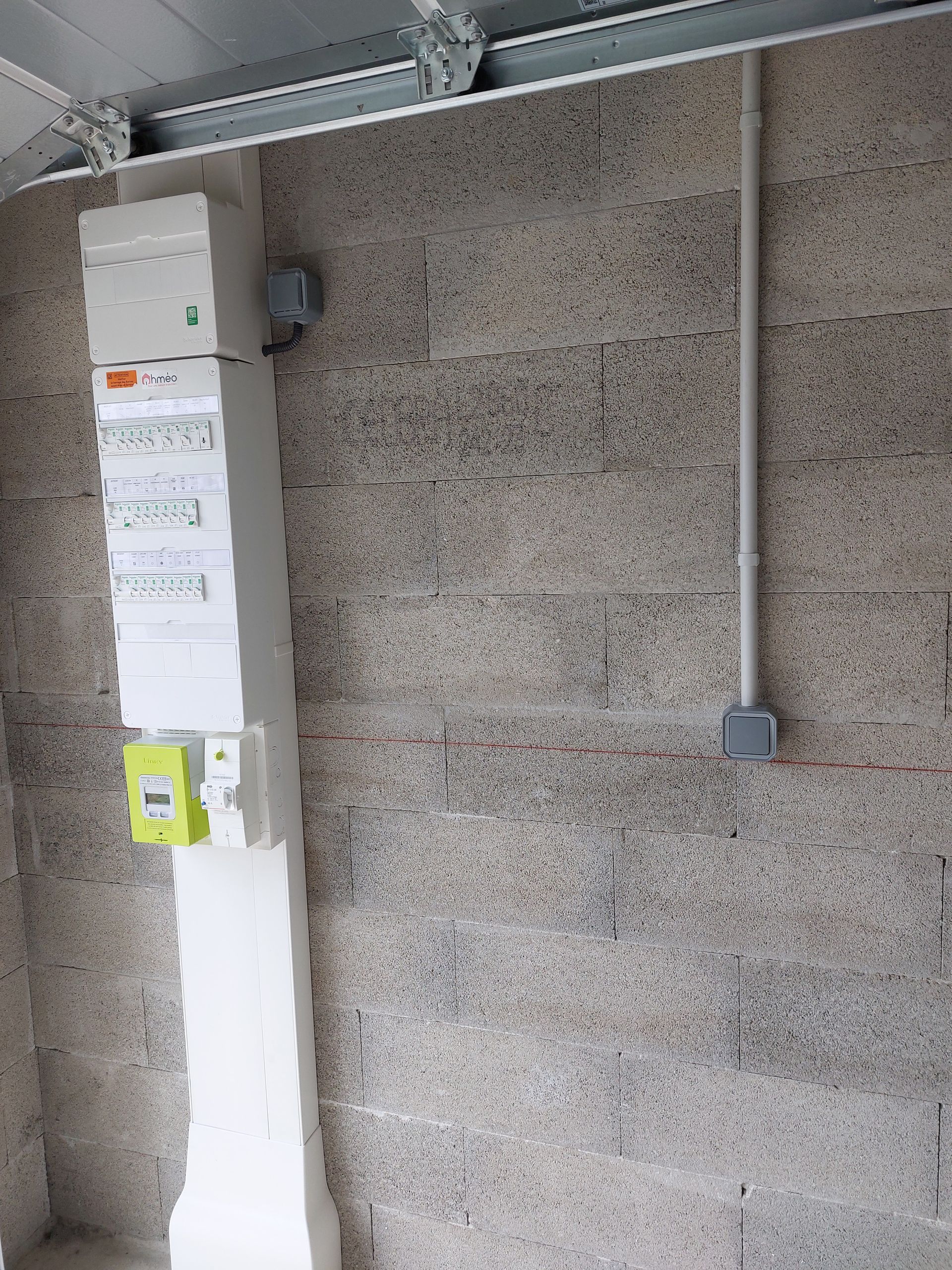 Tableau électrique et conduit sur un mur en parpaings.
