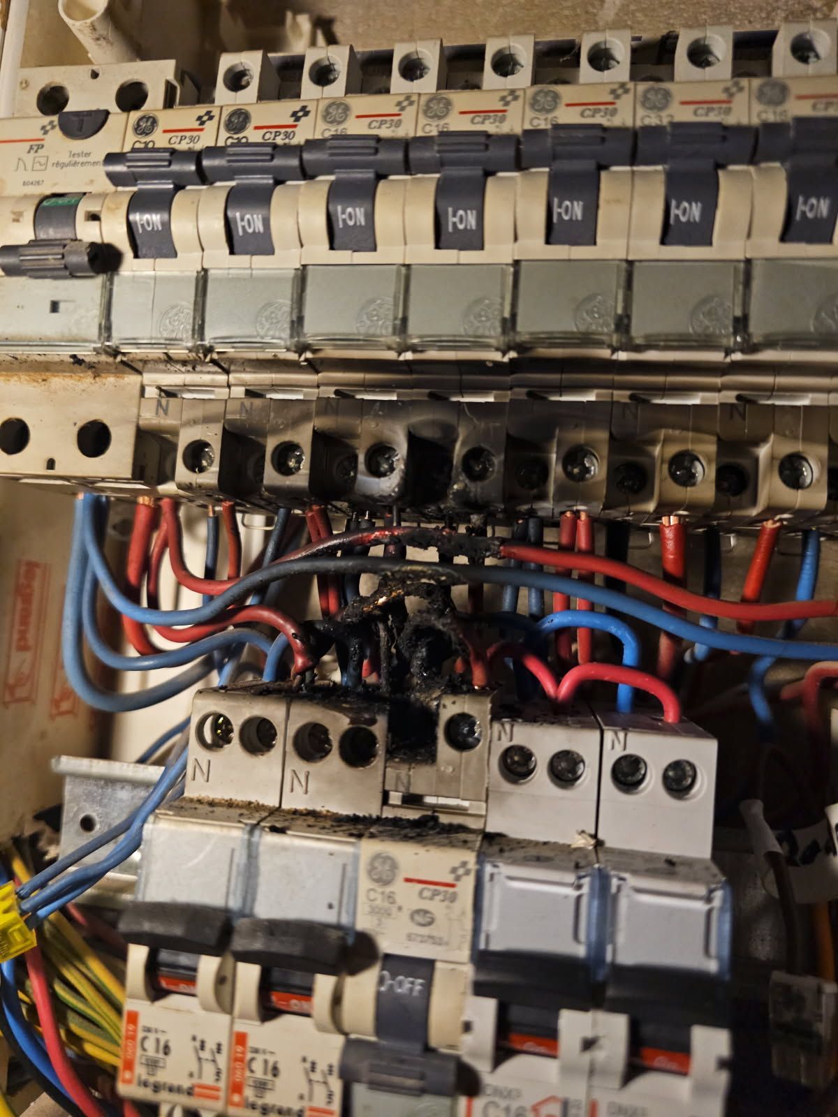 Tableau électrique endommagé : fils et disjoncteurs brûlés. La zone noircie indique un risque d’incendie.