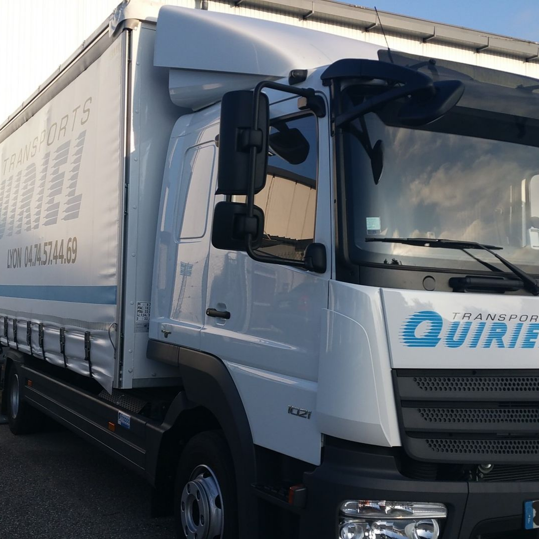 Camion blanc avec un logo bleu et blanc, garé à l'extérieur.