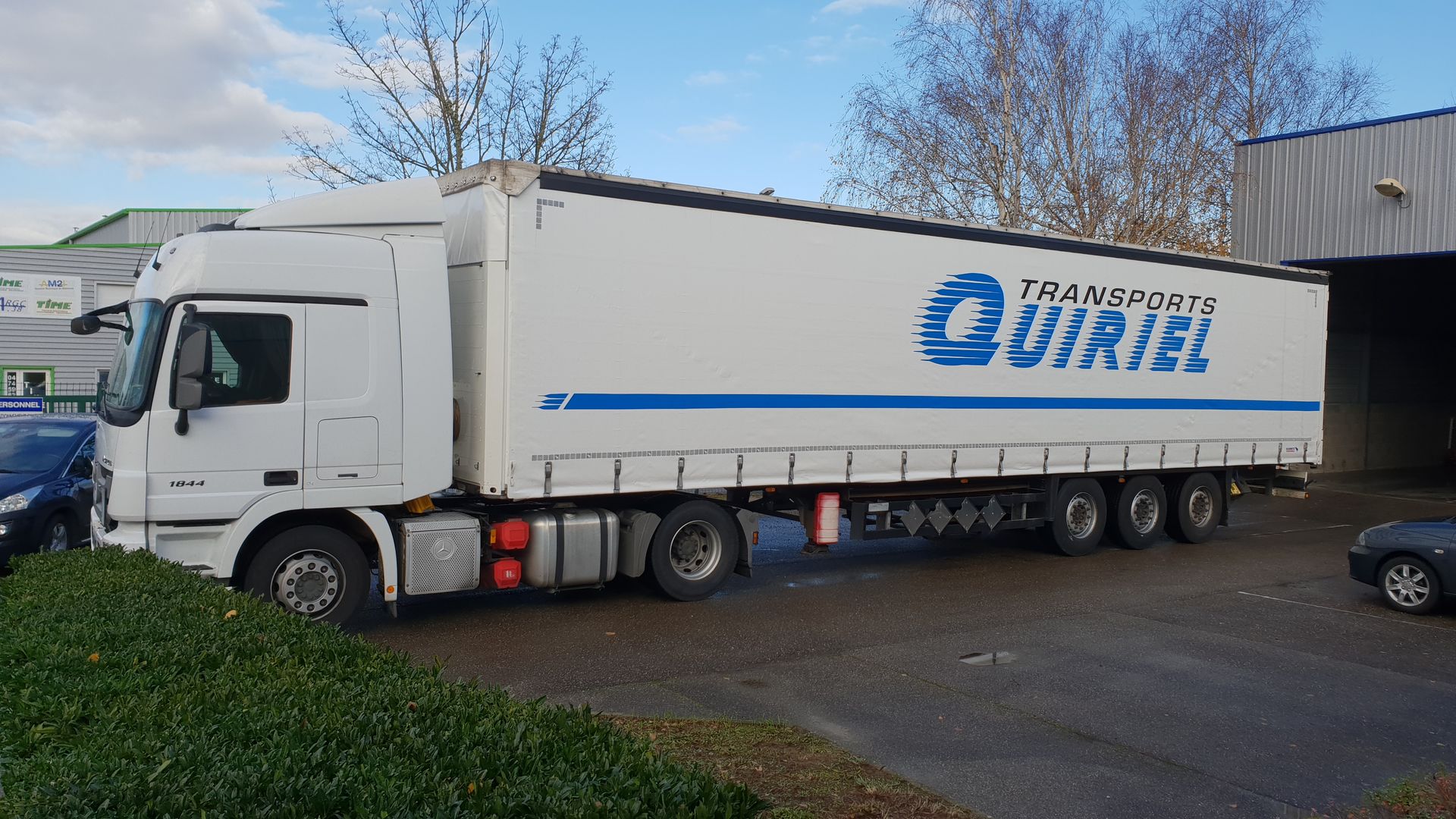 Camion blanc avec le logo Transports Uriel en bleu sur fond de ciel bleu.