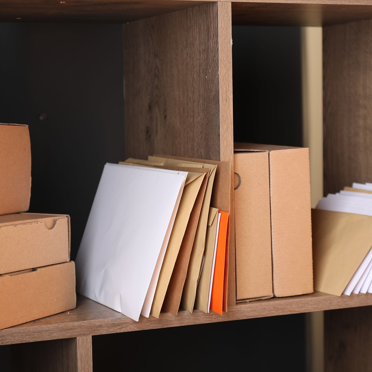 Étagère en bois avec enveloppes, boîtes et papiers empilés.