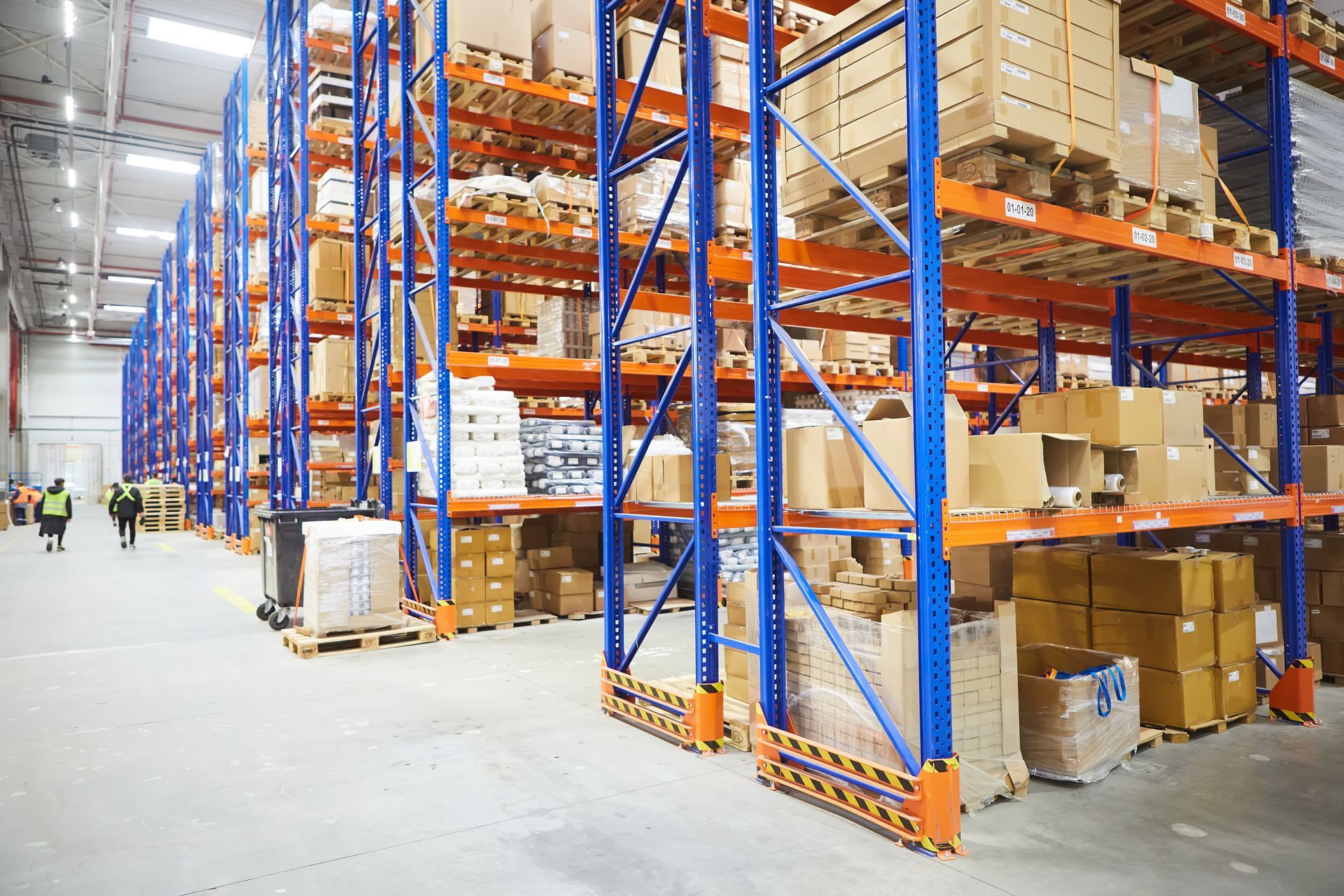 Intérieur d'entrepôt avec des boîtes en carton empilées au premier plan, des étagères en arrière-plan.