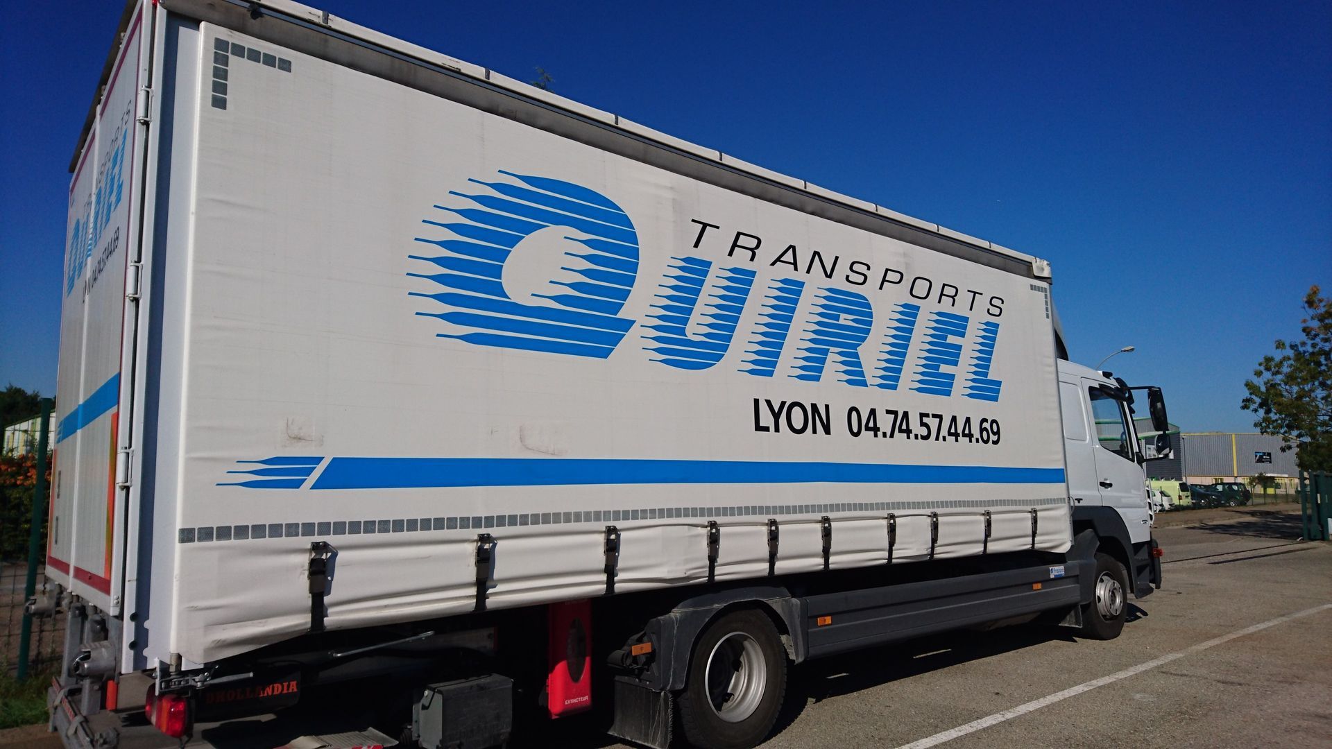 Camion blanc avec le logo Transports Uriel en bleu sur fond de ciel bleu.